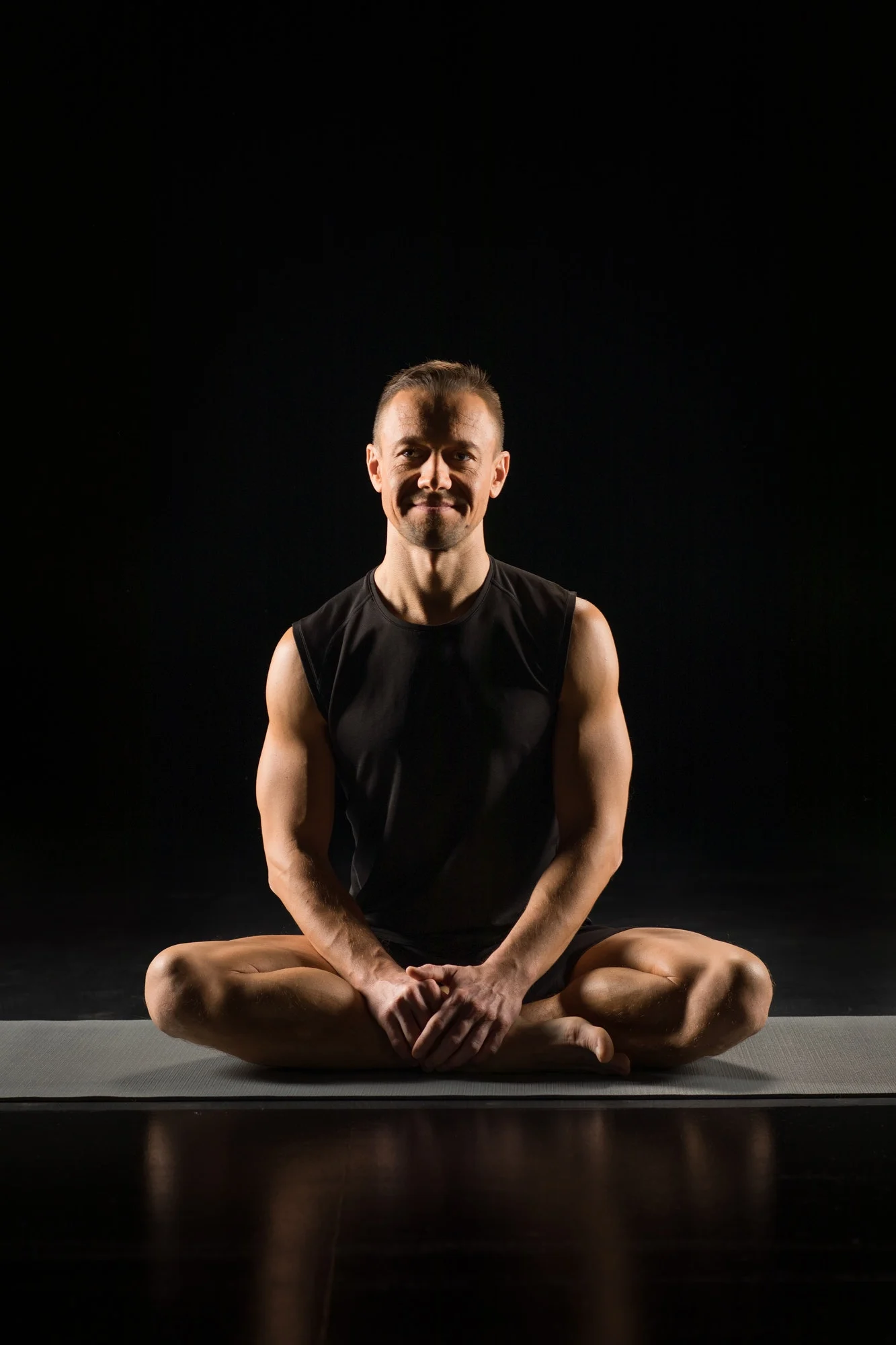 Young athletic man practicing yoga while sitting in lotus position and smiling at camera, isolated.